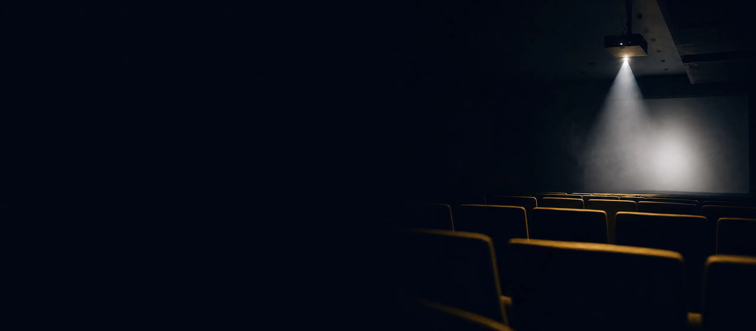 A projector throwing a single cone of light across a dark lecture hall toward a bright screen